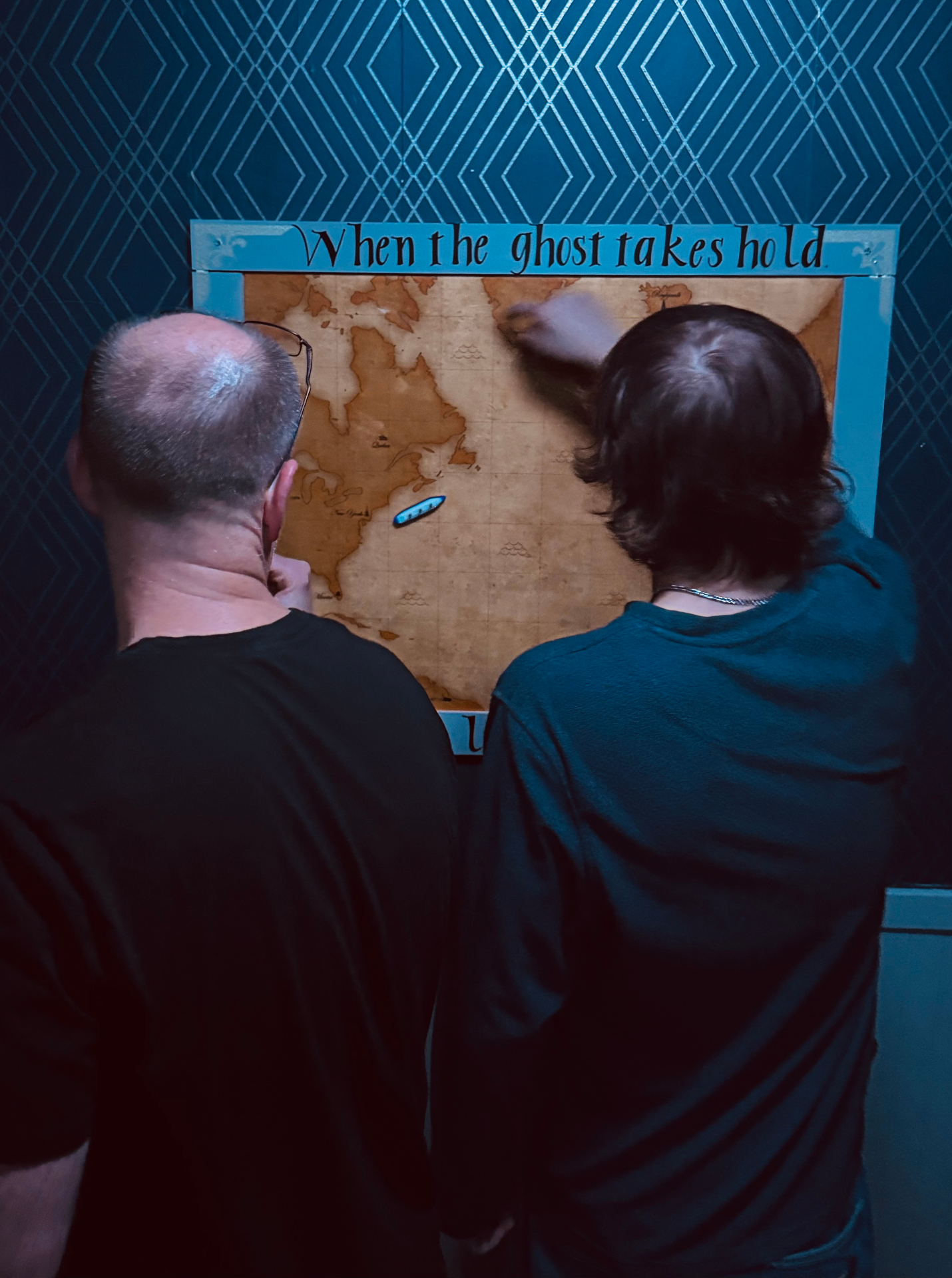 Two players examining a weathered map on a teal patterned wall inside the Abigail Rose room.