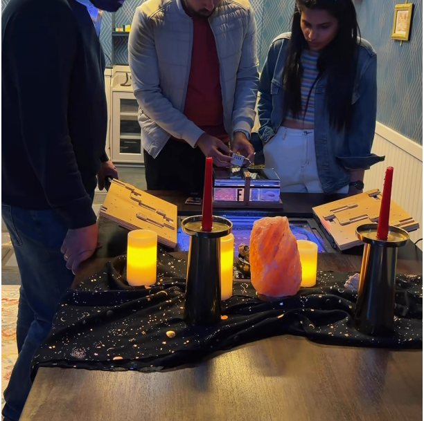 Players gather around a candlelit table with a salt lamp and glowing device inside The Restless Spirit of Abigail Rose escape room.